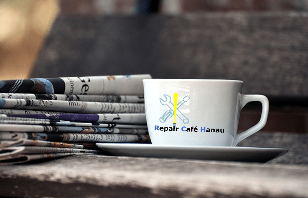 Tasse mit Repair Café Logo und Zeitungen.